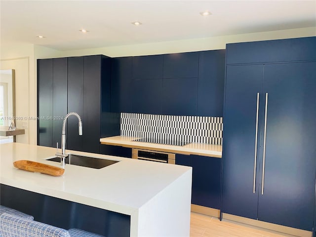 kitchen with blue cabinetry, light hardwood / wood-style flooring, sink, paneled built in fridge, and a center island with sink