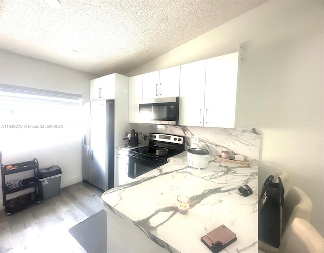 kitchen featuring lofted ceiling, white cabinets, stainless steel appliances, and light hardwood / wood-style floors