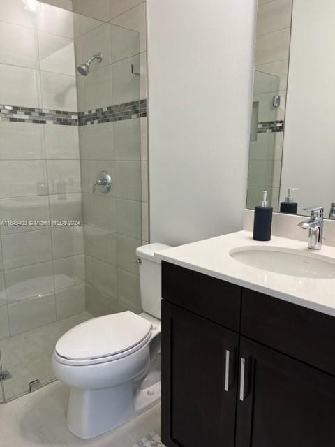 bathroom with tiled shower, vanity, toilet, and tile patterned flooring