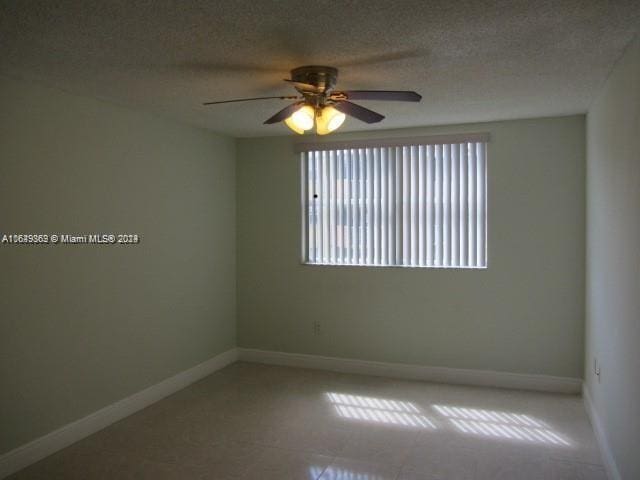 tiled empty room with ceiling fan, plenty of natural light, and a textured ceiling