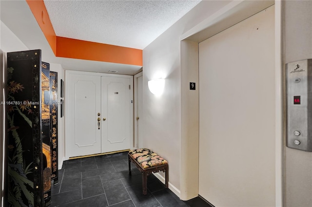 foyer with dark tile patterned flooring, a textured ceiling, and elevator