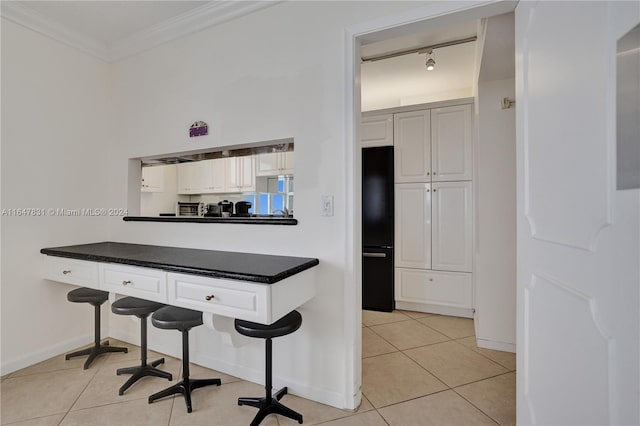 kitchen featuring a kitchen breakfast bar, light tile patterned floors, ornamental molding, black fridge, and track lighting