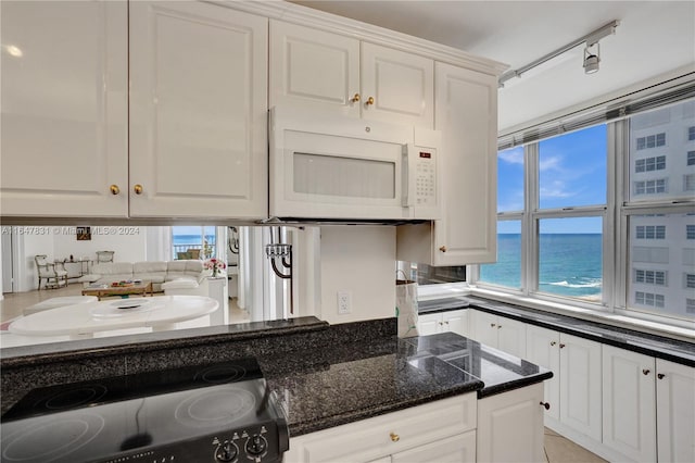 kitchen featuring dark stone countertops, white cabinetry, a wealth of natural light, and a water view