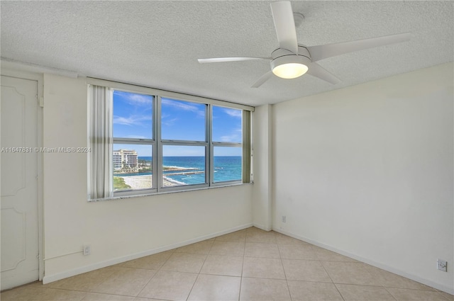 unfurnished room featuring a water view, ceiling fan, light tile patterned floors, and a textured ceiling