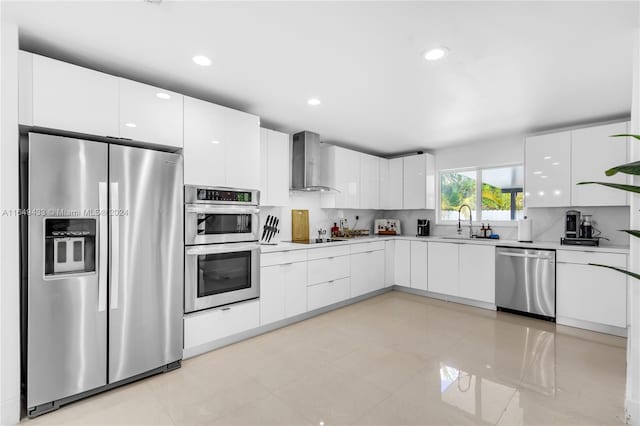 kitchen featuring sink, white cabinetry, wall chimney range hood, backsplash, and appliances with stainless steel finishes