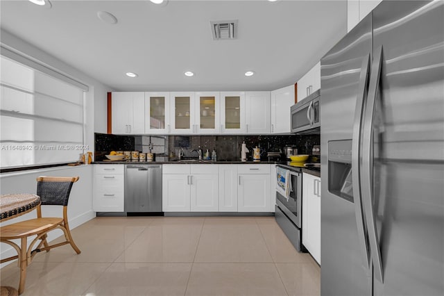 kitchen featuring white cabinets, backsplash, light tile patterned floors, appliances with stainless steel finishes, and sink