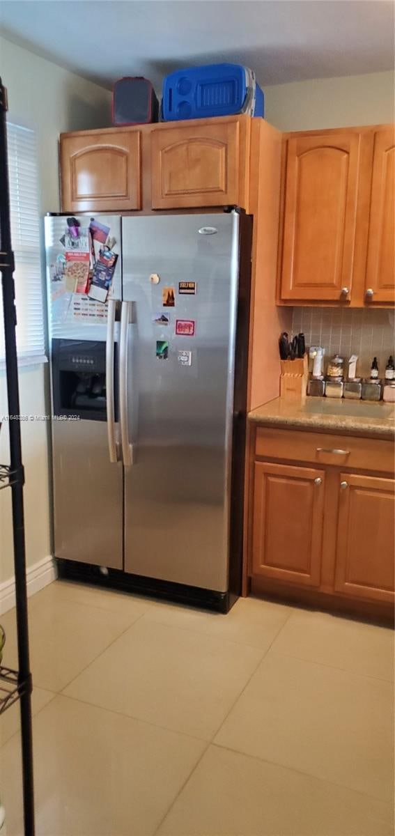 kitchen featuring stainless steel fridge, light tile patterned floors, and backsplash