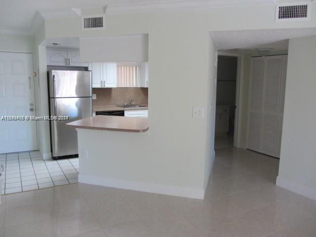 kitchen featuring stainless steel refrigerator, light tile patterned floors, kitchen peninsula, decorative backsplash, and white cabinets