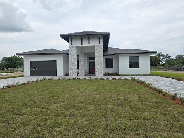 prairie-style house featuring a front lawn, decorative driveway, a garage, and stucco siding