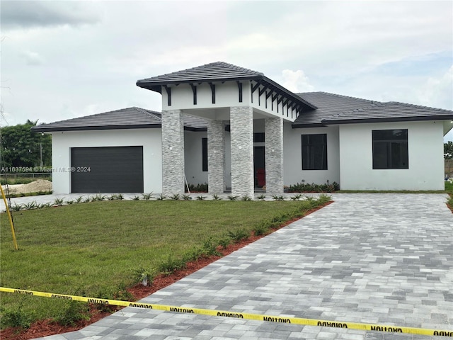 prairie-style house with decorative driveway, a garage, a front yard, and stucco siding