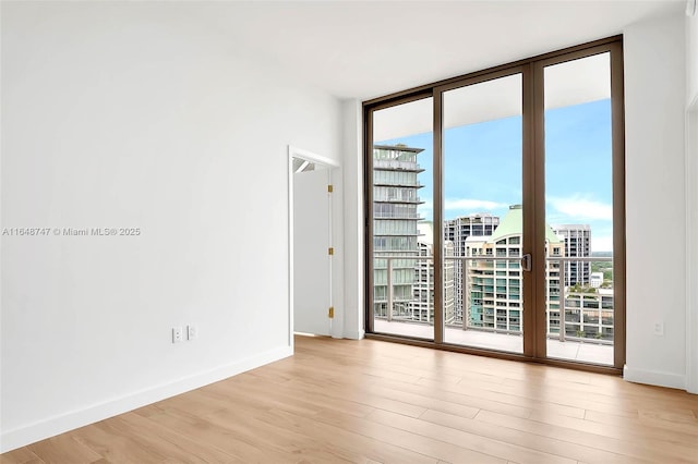 spare room featuring light wood finished floors, baseboards, expansive windows, a city view, and a healthy amount of sunlight