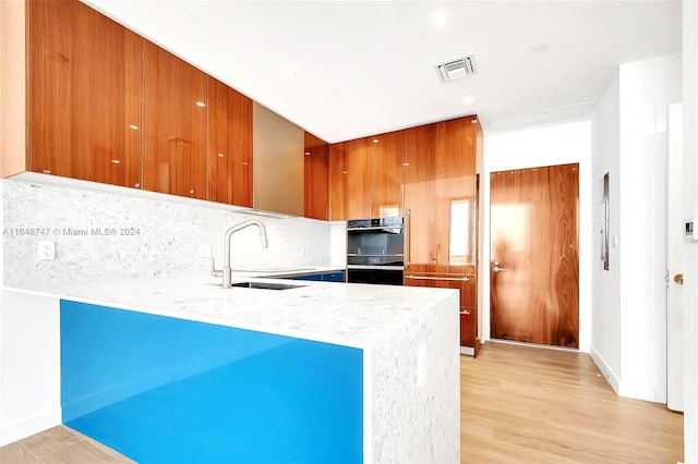 kitchen with sink, kitchen peninsula, light stone countertops, light hardwood / wood-style floors, and decorative backsplash