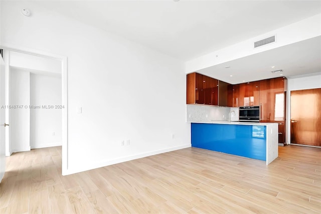 kitchen with light hardwood / wood-style floors, black oven, kitchen peninsula, and tasteful backsplash