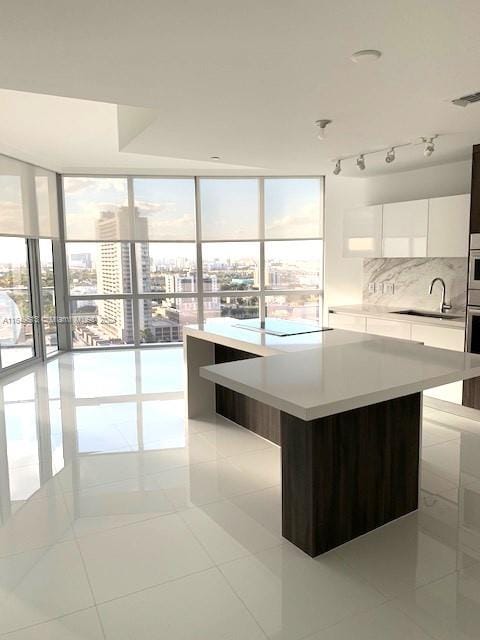 kitchen with light tile patterned floors, white cabinetry, track lighting, expansive windows, and decorative backsplash