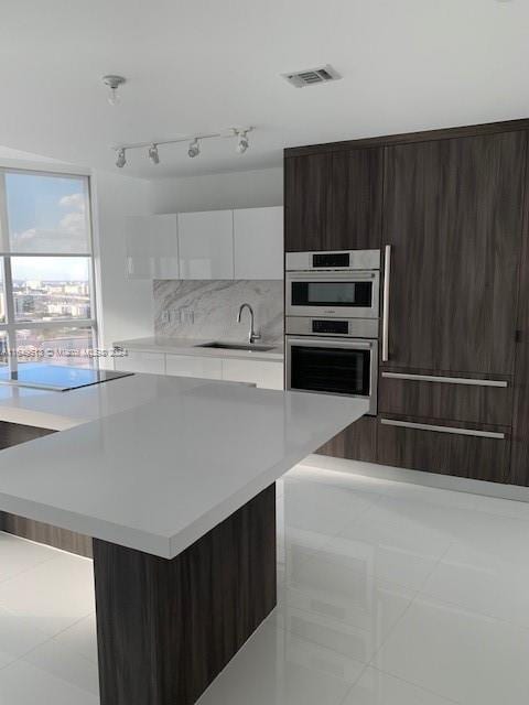 kitchen featuring white cabinets, backsplash, light tile patterned floors, sink, and rail lighting