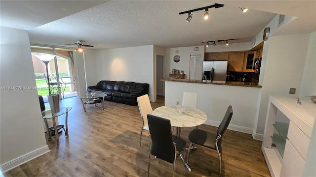 dining room with ceiling fan, hardwood / wood-style flooring, rail lighting, and a textured ceiling