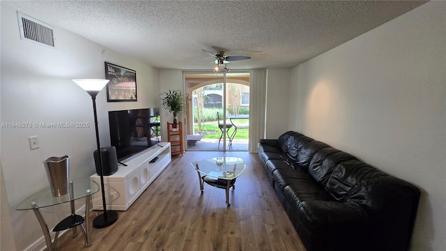 living room with ceiling fan, wood-type flooring, and a textured ceiling