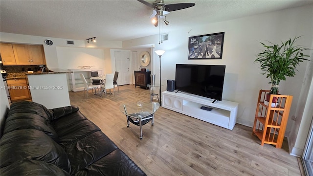 living room featuring ceiling fan, a textured ceiling, and light hardwood / wood-style floors