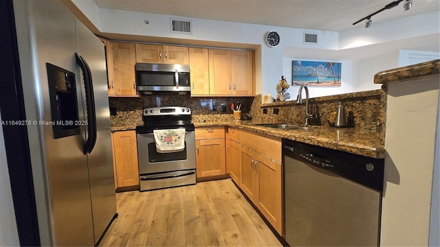 kitchen featuring appliances with stainless steel finishes, tasteful backsplash, sink, dark stone counters, and light hardwood / wood-style floors