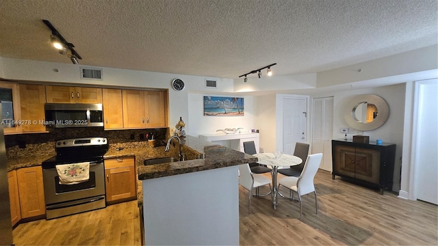 kitchen featuring sink, stainless steel appliances, light hardwood / wood-style floors, a textured ceiling, and decorative backsplash