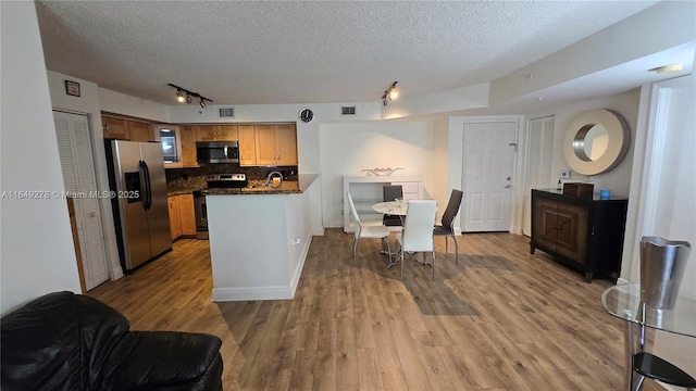 kitchen featuring appliances with stainless steel finishes, tasteful backsplash, rail lighting, light hardwood / wood-style floors, and a textured ceiling