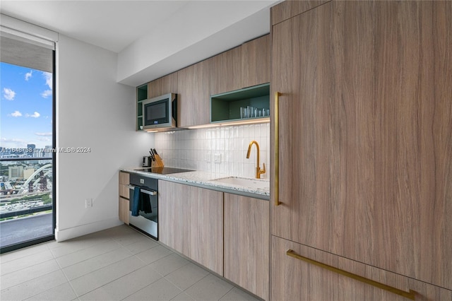 kitchen featuring a wealth of natural light, light stone counters, stainless steel appliances, and sink