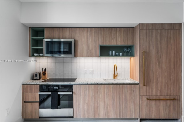 kitchen with black appliances, light stone counters, sink, and decorative backsplash