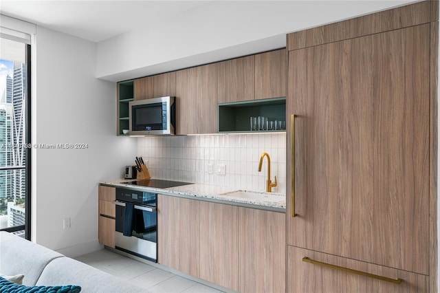 kitchen with light tile patterned floors, appliances with stainless steel finishes, light stone countertops, sink, and tasteful backsplash