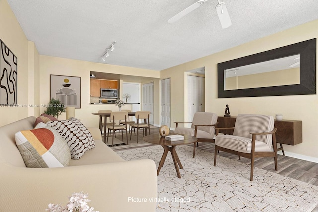 living room with track lighting, hardwood / wood-style floors, ceiling fan, and a textured ceiling