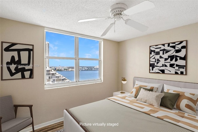 bedroom with a textured ceiling, a water view, hardwood / wood-style floors, and ceiling fan