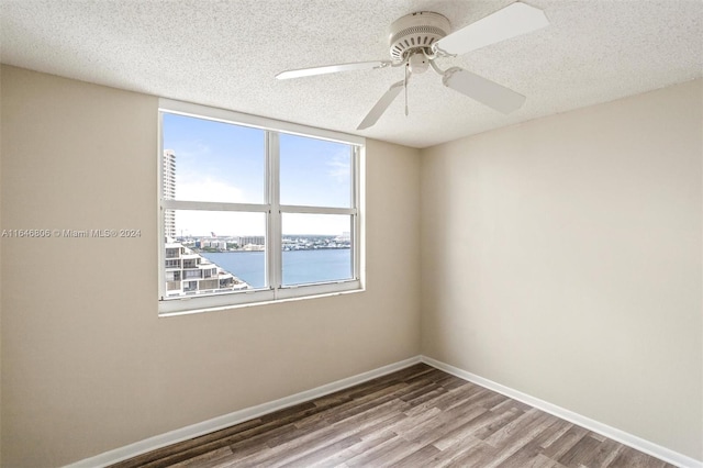 unfurnished room featuring a water view, ceiling fan, wood-type flooring, and a textured ceiling