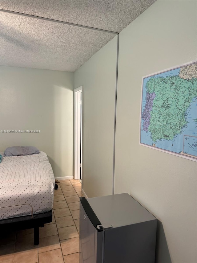 bedroom featuring a textured ceiling, stainless steel fridge, and light tile patterned floors