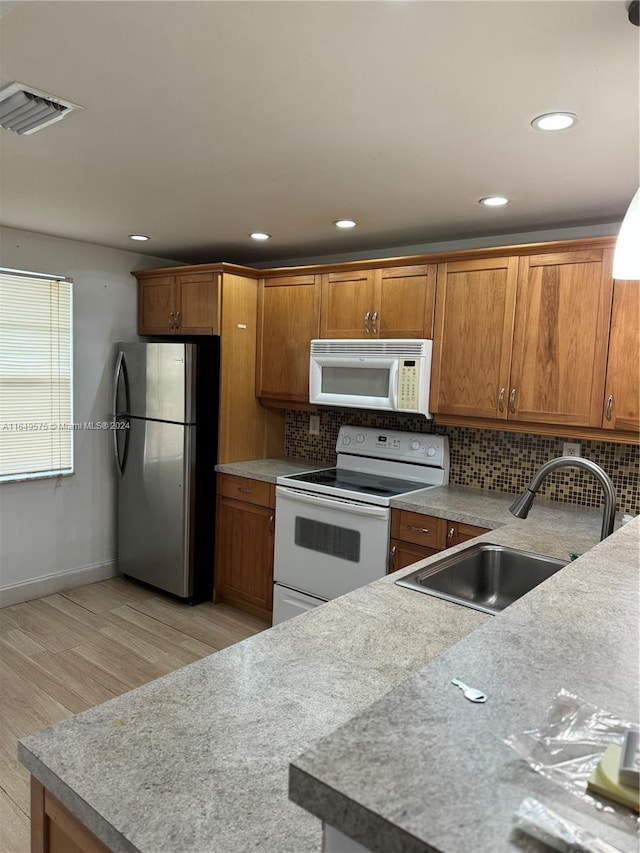 kitchen with sink, backsplash, light hardwood / wood-style floors, and white appliances