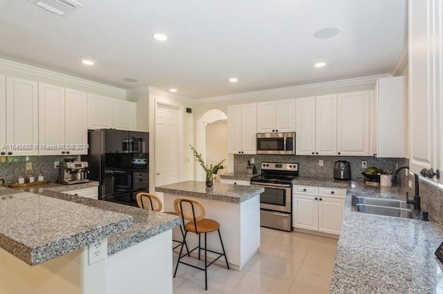 kitchen with stainless steel appliances, a center island, sink, a breakfast bar, and white cabinetry