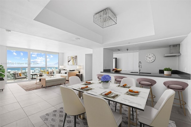 tiled dining space with a tray ceiling, sink, and a water view