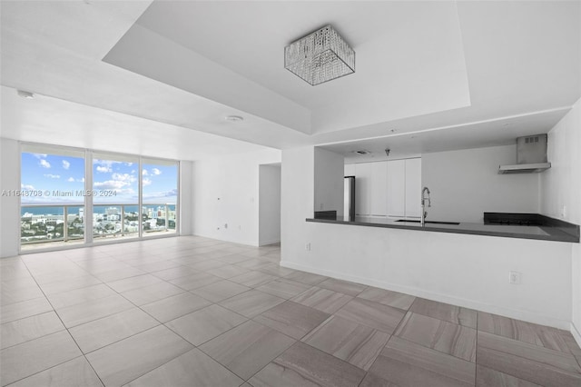 unfurnished living room featuring light tile patterned floors, a raised ceiling, and sink