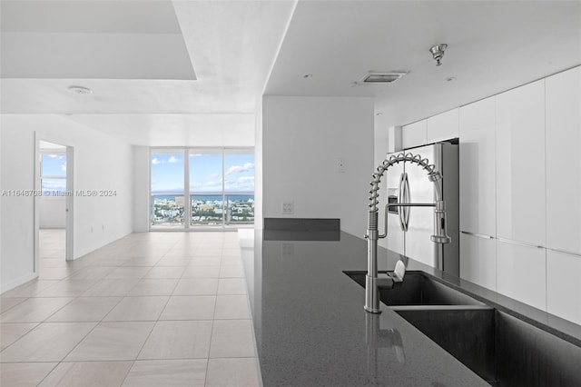 kitchen featuring white cabinets, light tile patterned floors, sink, stainless steel fridge with ice dispenser, and a wall of windows