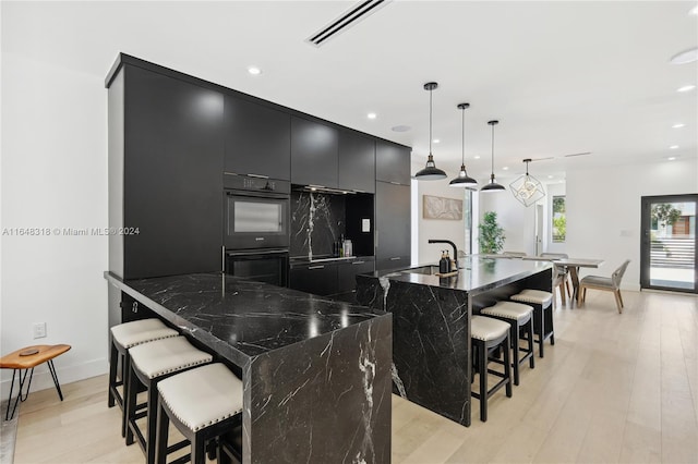 kitchen featuring light wood-type flooring, sink, a large island, pendant lighting, and a breakfast bar