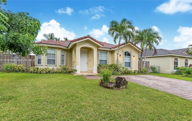 mediterranean / spanish-style home featuring fence, a tile roof, a front yard, and stucco siding
