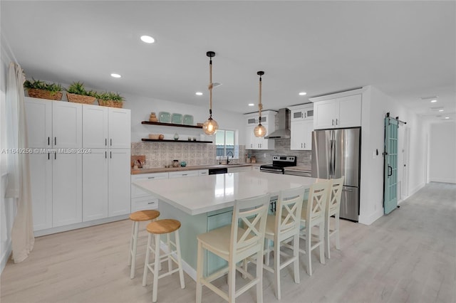 kitchen featuring light wood-type flooring, stainless steel appliances, a center island, wall chimney exhaust hood, and white cabinets