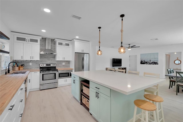 kitchen with stainless steel appliances, white cabinetry, sink, wall chimney range hood, and tasteful backsplash