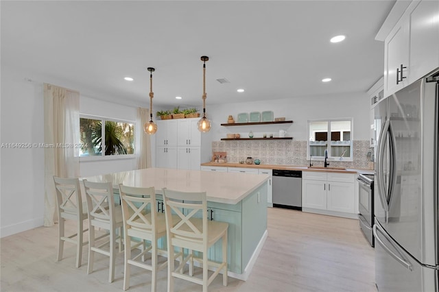 kitchen featuring backsplash, decorative light fixtures, appliances with stainless steel finishes, white cabinetry, and a kitchen island