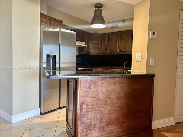 kitchen featuring dark stone counters, light tile patterned floors, stove, kitchen peninsula, and stainless steel refrigerator with ice dispenser