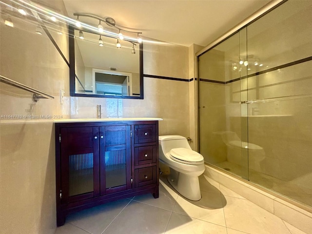 bathroom featuring a shower with door, vanity, tile walls, toilet, and tile patterned floors