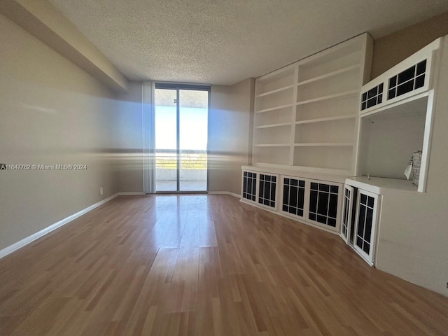 unfurnished room featuring a textured ceiling, hardwood / wood-style flooring, floor to ceiling windows, and built in shelves