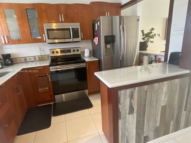 kitchen featuring stainless steel appliances, glass insert cabinets, light countertops, and brown cabinets