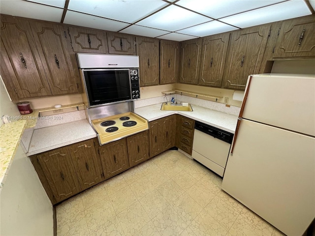 kitchen featuring dark brown cabinetry, white appliances, a sink, light countertops, and light floors