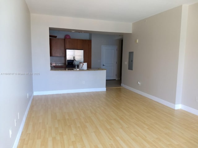 unfurnished living room with sink, electric panel, and light hardwood / wood-style flooring