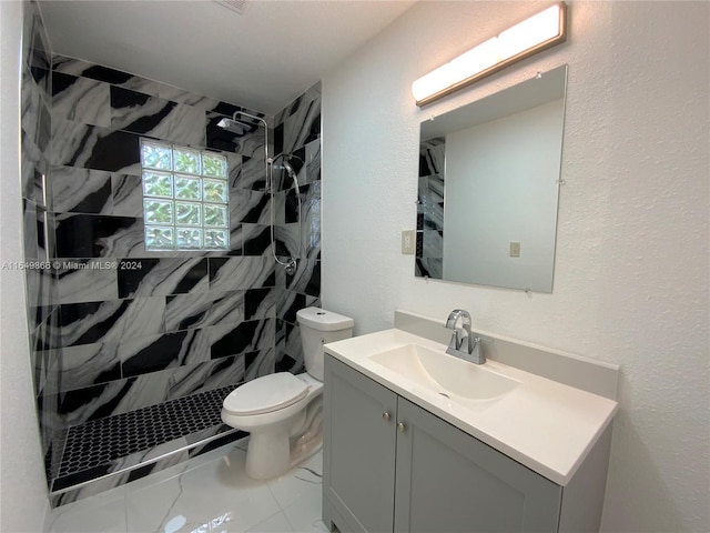 bathroom with tile patterned flooring, toilet, a tile shower, and vanity