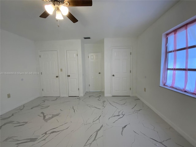 unfurnished bedroom with ceiling fan, light tile patterned floors, and two closets